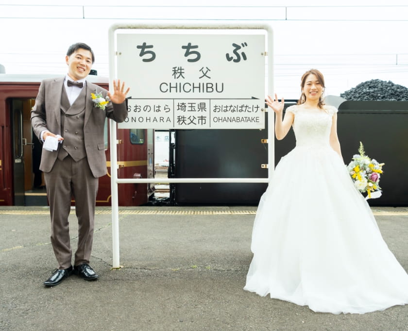 新郎新婦が秩父駅の表札横でポーズを取っている写真